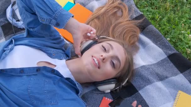 Smile girl student listening music outdoor, lying on grass and relaxing - Filmagem, Vídeo