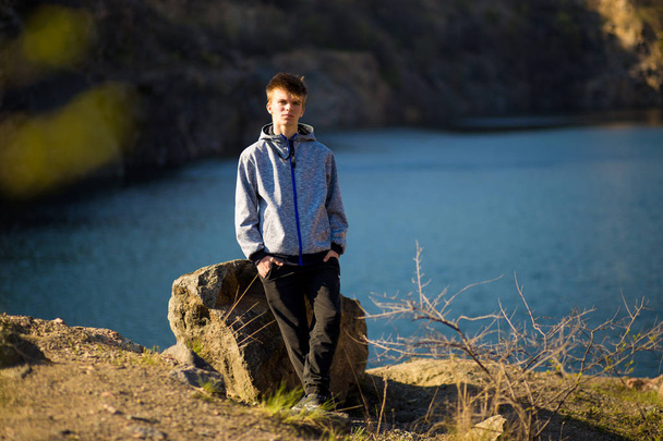 Mladý muž stojí u skály pobřeží jezera a dívá se na obzor. Sebevědomí v budoucnosti - Fotografie, Obrázek