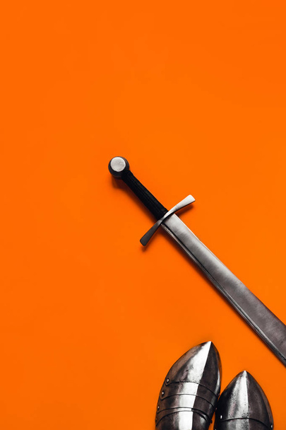 Sabatonlar ve turuncu bir arka plan üzerinde bir kılıç. - Fotoğraf, Görsel