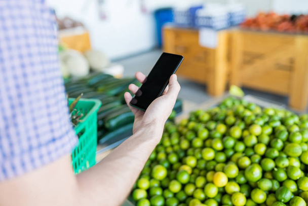 Περικομμένη εικόνα του ανθρώπου που κρατά smartphone με κενή οθόνη, ενώ αγορές για λεμόνια στο κατάστημα - Φωτογραφία, εικόνα