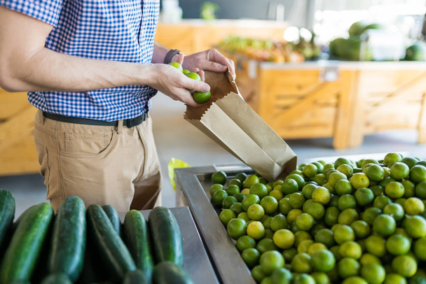 Midsection del hombre recogiendo limones verdes en una pequeña bolsa de papel mientras hace compras en el centro comercial
 - Foto, imagen
