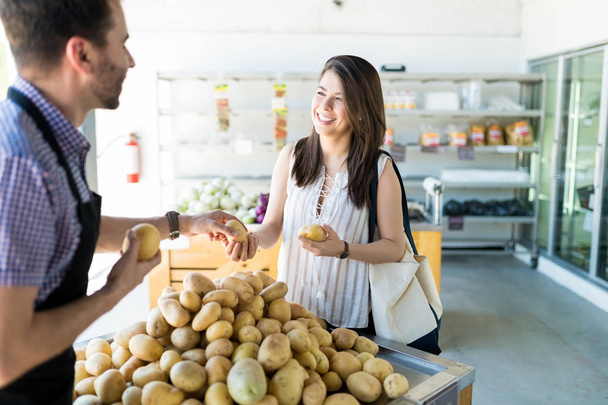 Усміхнений покупець отримує допомогу від власника магазину у виборі картоплі в супермаркеті
 - Фото, зображення