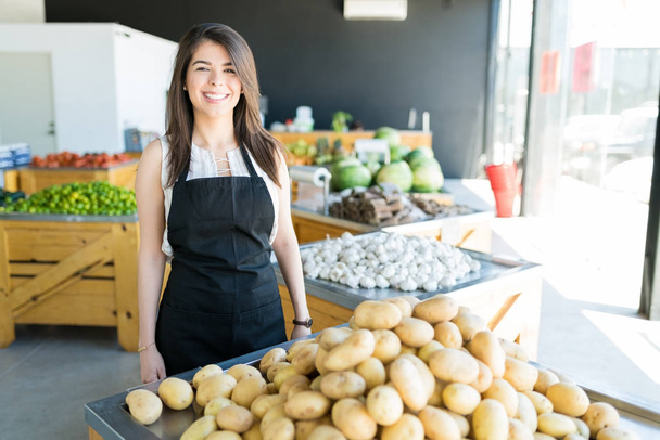 Beautiful smiling female owner standing by heap of potatoes in organic store - Photo, Image