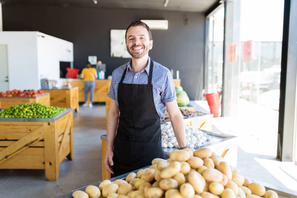 Hymyilevä myymälän johtaja yllään esiliina myydessään vihanneksia luomumarkkinoilla
 - Valokuva, kuva