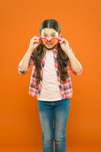 She is a smart one. Little smart girl on orange background. Adorable child with smart look through fancy glasses. Fashionable small kid wearing smart glasses - Photo, Image