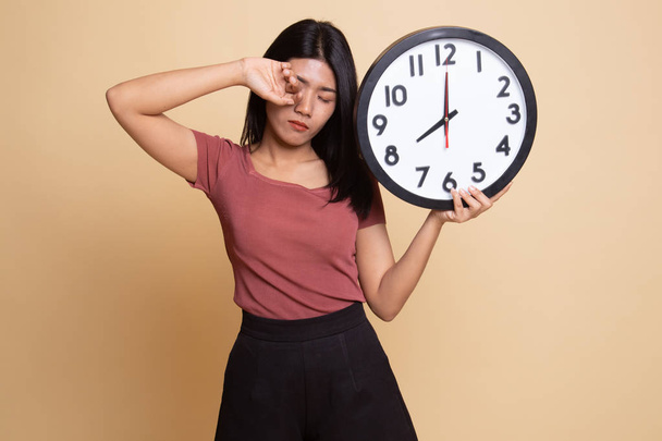 Sleepy young Asian woman with a clock in the morning. - Foto, Imagen