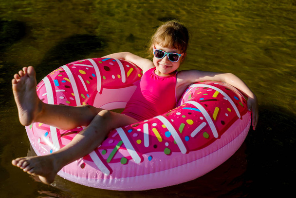 Girl in a pink bathing suit and sunglasses swimming on an inflatable ring. - Foto, afbeelding