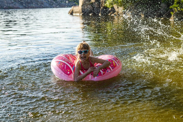 Child in a pink bathing suit with an inflatable ring swims in the river. - Foto, afbeelding