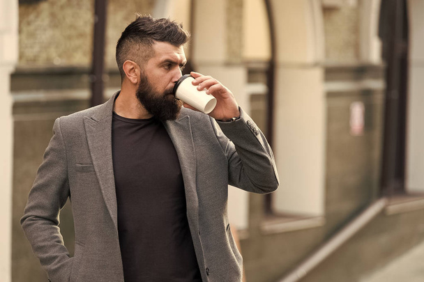 The best time to drink coffee. Bearded man drinking morning coffee. Businessman in hipster style holding takeaway coffee. Hipster with disposable paper cup walking in city. Day begins with coffee - Фото, изображение