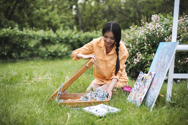 Bir genç mutlu moda Asyalı kadın şehir parkı açık doğada sıcak güneşli bir günde bir şelon bir resim boyama başlıyor. Sanat terapisi, dinlenmek ve hobi kavramı, tatil dinlenme günü - Fotoğraf, Görsel