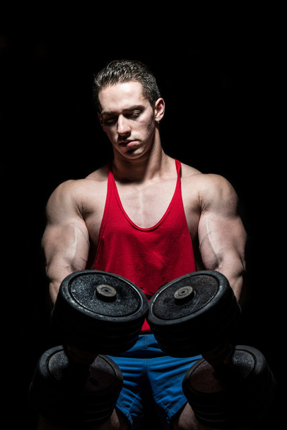 young bodybuilder posing with dumbbell at the bench on black bac - Foto, Imagem