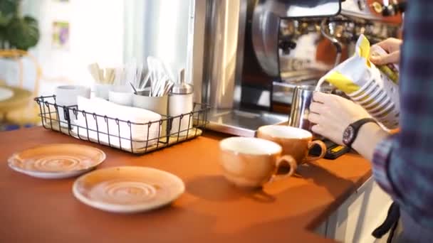 Seitenansicht eines professionellen Baristas, der im Café frische Milch in den Krug gibt und Heißgetränke zubereitet. Kunst. Kaffeemaschine, Tassen und Teller und andere Dinge im Kaffeehaus. - Filmmaterial, Video