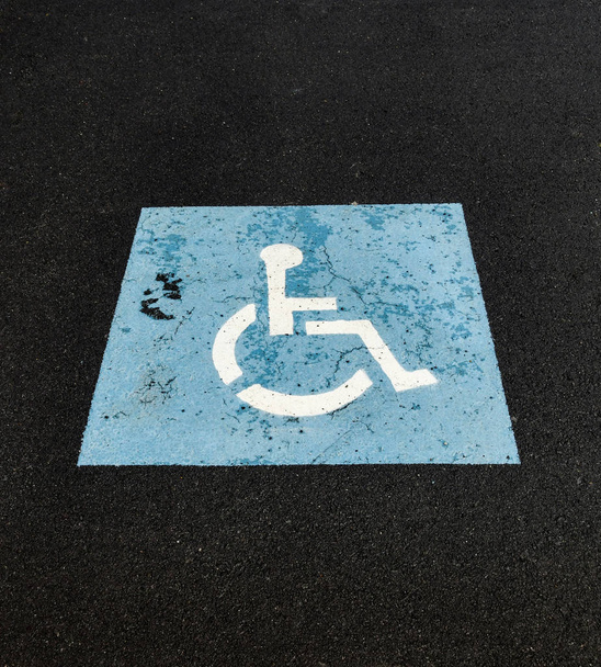 Κλείσιμο ενός συμβόλου αναπηρικής πολυθρόνας που είναι ζωγραφισμένο στην επιφάνεια ενός πάρκου αυτοκινήτων για να υποδηλώσει ένα χώρο στάθμευσης αυτοκινήτων για άτομα με ειδικές ανάγκες, - Φωτογραφία, εικόνα