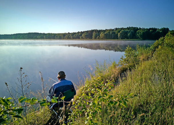 Un hombre pescando en la orilla de un hermoso lago
. - Foto, imagen