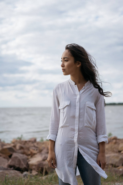 Красива Азіатська жінка, що ходить уздовж пляжу, дихає свіжим повітрям, думаючи, насолоджуючись видом природи, відпочиваючи біля річки. Пенсивна Корейська дівчина шукає натхнення на відкритому повітрі  - Фото, зображення