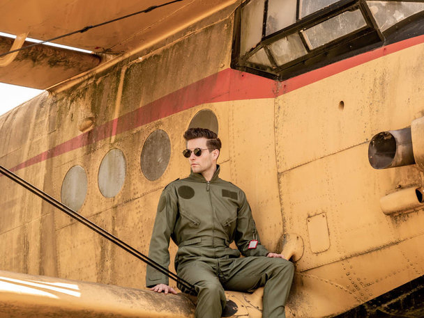 Bir uçağın kanadında oturan yakışıklı bir genç pilot - Fotoğraf, Görsel