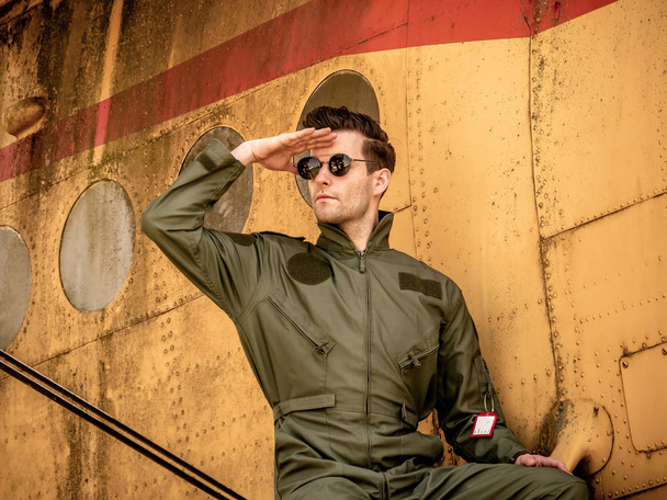 A handsome young pilot sitting on the wing of a plane and coveri - Foto, afbeelding