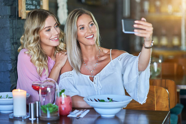 Two girl friends eating lunch in restaurant and using smartphone - Fotó, kép