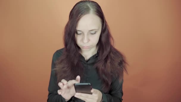 Young woman holding mobile phone in hand on orange background. Female typing a message on a smartphone - Video