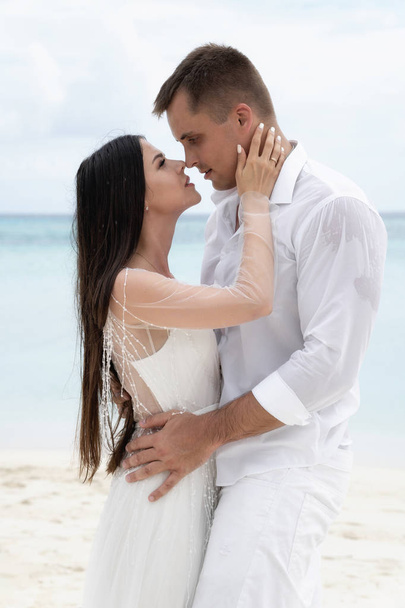 Newlyweds are hugging on a gorgeous beach with white sand and turquoise water. - Photo, image