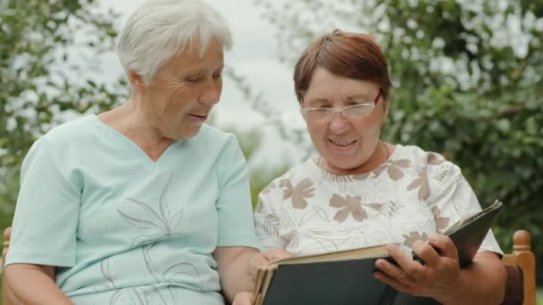 Two elderly women view photos outdoors - Footage, Video
