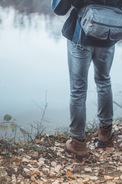 Мужчина в легких джинсах и сапогах стоит у реки. Вроде ног. Осень. Добрый вечер. Крупный план
 - Фото, изображение