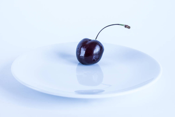 Burgundy cherry berry on a white plate close-up on a white background - Foto, Imagen