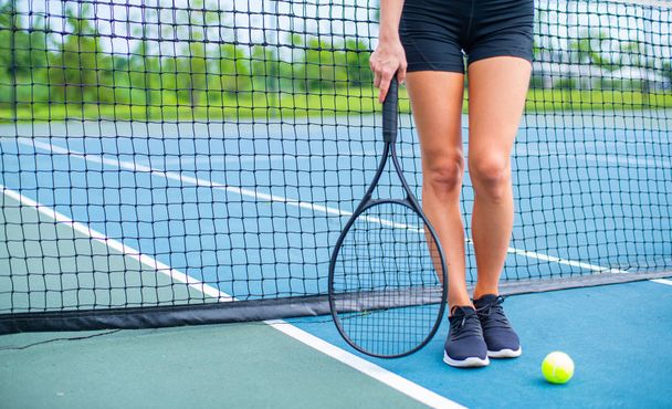 Beautiful woman legs with tennis racket on tennis court - 写真・画像