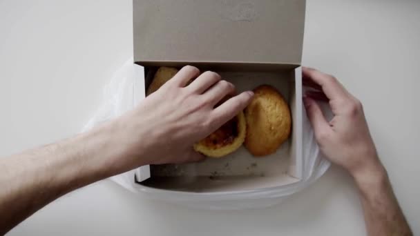Mans hand takes bun out of white paper box in plastic bag with other buns. - Footage, Video