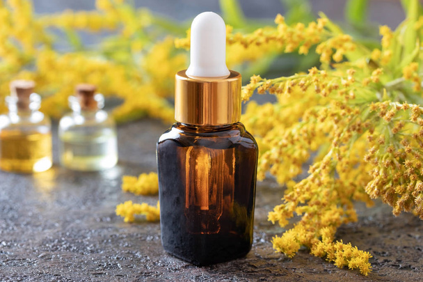 Una botella de aceite esencial de varilla de oro con planta fresca
 - Foto, Imagen