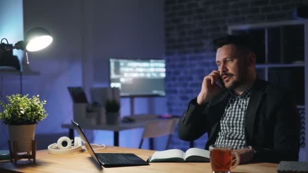 Stressed entrepreneur talking on mobile phone at night in office working late - Video, Çekim