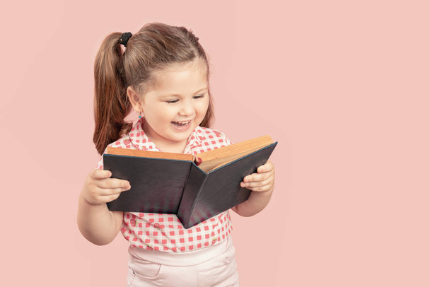 Little Cute Girl Reading Book And Smiling on Pink Background - Fotoğraf, Görsel