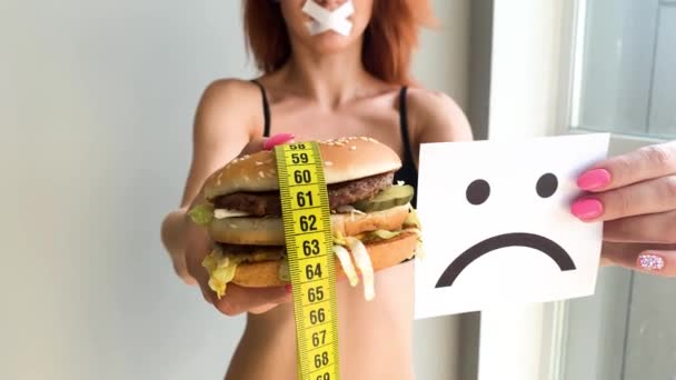 Dieta. Retrato de una mujer quiere comer una hamburguesa, pero una boca pegada, una noción de dieta, comida poco saludable, una voluntad en la nutrición
 - Imágenes, Vídeo
