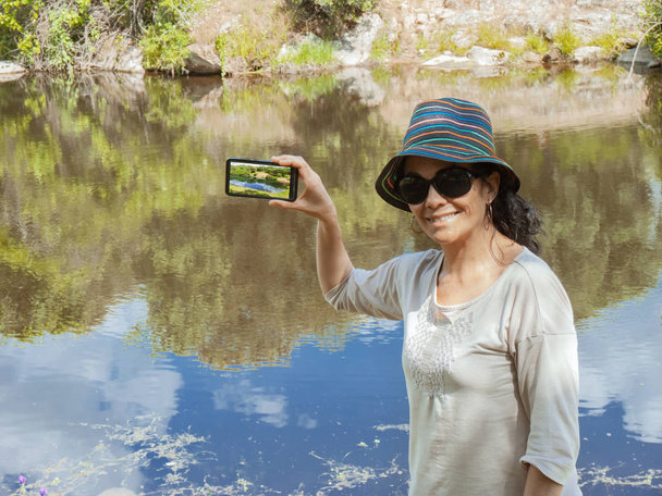 Brunette nainen tekee valokuvan hänen matkapuhelin katselee kameraa
 - Valokuva, kuva