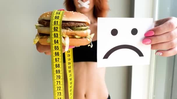 Dieet. Portret van een vrouw wil een hamburger te eten, maar een gelijmde mond, een begrip van dieet, ongezond voedsel, een wil in voeding - Video