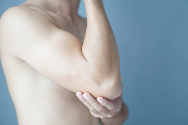 Крупный план рука человека держа локоть с болью с синим фоном, здравоохранение и медицинская концепция
 - Фото, изображение