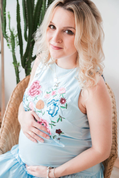 pregnant woman in a blue dress sitting in a wicker chair - Photo, image