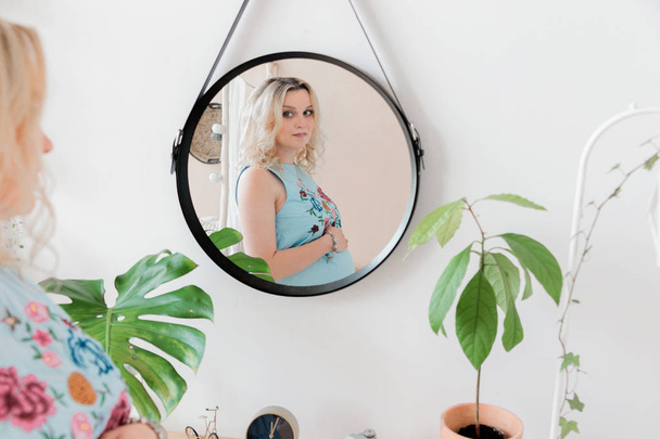 fille enceinte blonde dans une robe bleue regarde dans le miroir
 - Photo, image