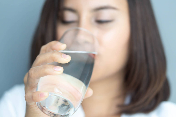 Κοντινό πάνω γυναίκα πίνοντας καθαρό νερό από γυαλί με μπλε φόντο, επιλεκτική εστίαση - Φωτογραφία, εικόνα