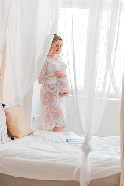 беременная женщина стоит у кровати и обнимает живот
 - Фото, изображение