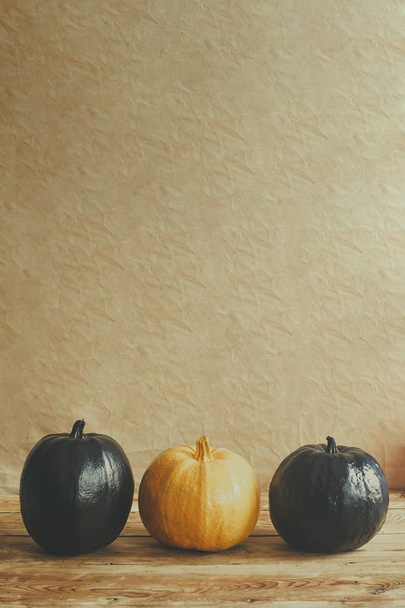 Farbige Halloween-Kürbisse auf Holzschreibtisch. Unterschied. Allein unter den anderen. einzelner orangefarbener Kürbis in einer Reihe schwarzer Kürbisse - Foto, Bild