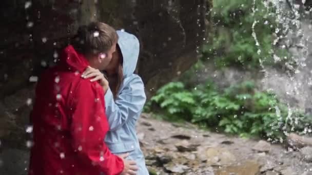 Les amoureux de papa en vestes se tiennent sous l'eau de la cascade et s'embrassent passionnément
.  - Séquence, vidéo