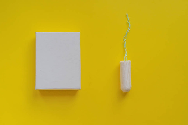 Menstruationsperiode. Hygieneschutz für Frauen. Baumwolltampon in einer weißen Schachtel auf gelbem Hintergrund. Kopierraum und Attrappe - Foto, Bild