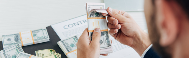 prise de vue panoramique d'un homme d'affaires tenant des billets en dollars près d'un contrat au bureau
  - Photo, image