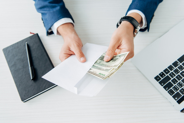 top view of man holding envelope with money near laptop on table  - Φωτογραφία, εικόνα