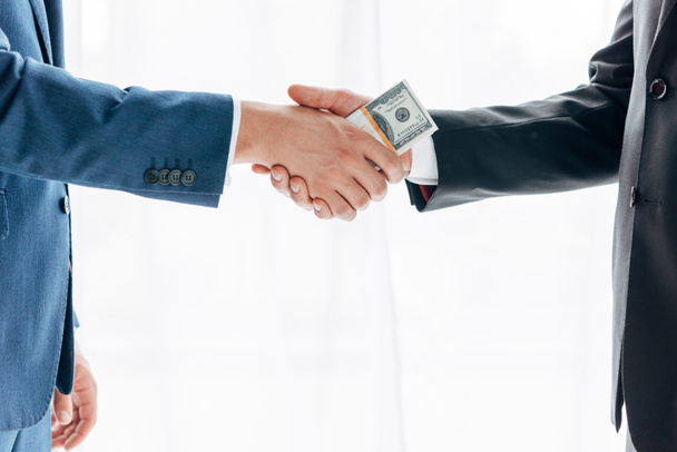 cropped view of man giving bribe to business partner and shaking hands on white - Foto, Imagen
