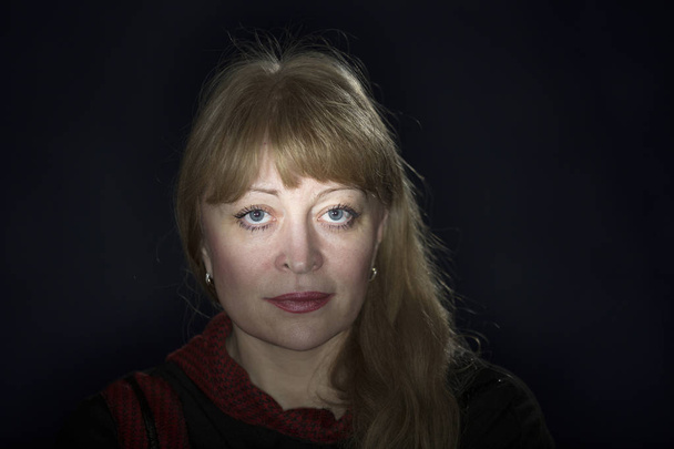 Porträt einer 50-jährigen Blondine vor dunklem Hintergrund - Foto, Bild