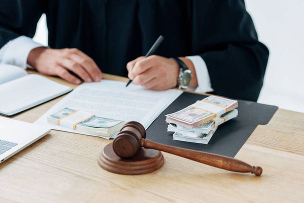 cropped view of judge signing document near money and gavel  - Фото, изображение
