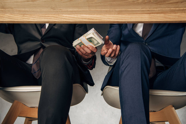 cropped view businessman giving bribe to business partner while sitting on chair  - 写真・画像