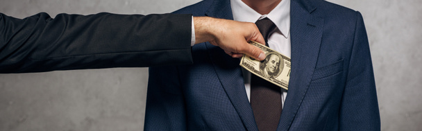 panoramic shot of man putting cash in pocket of business partner on grey  - Photo, image